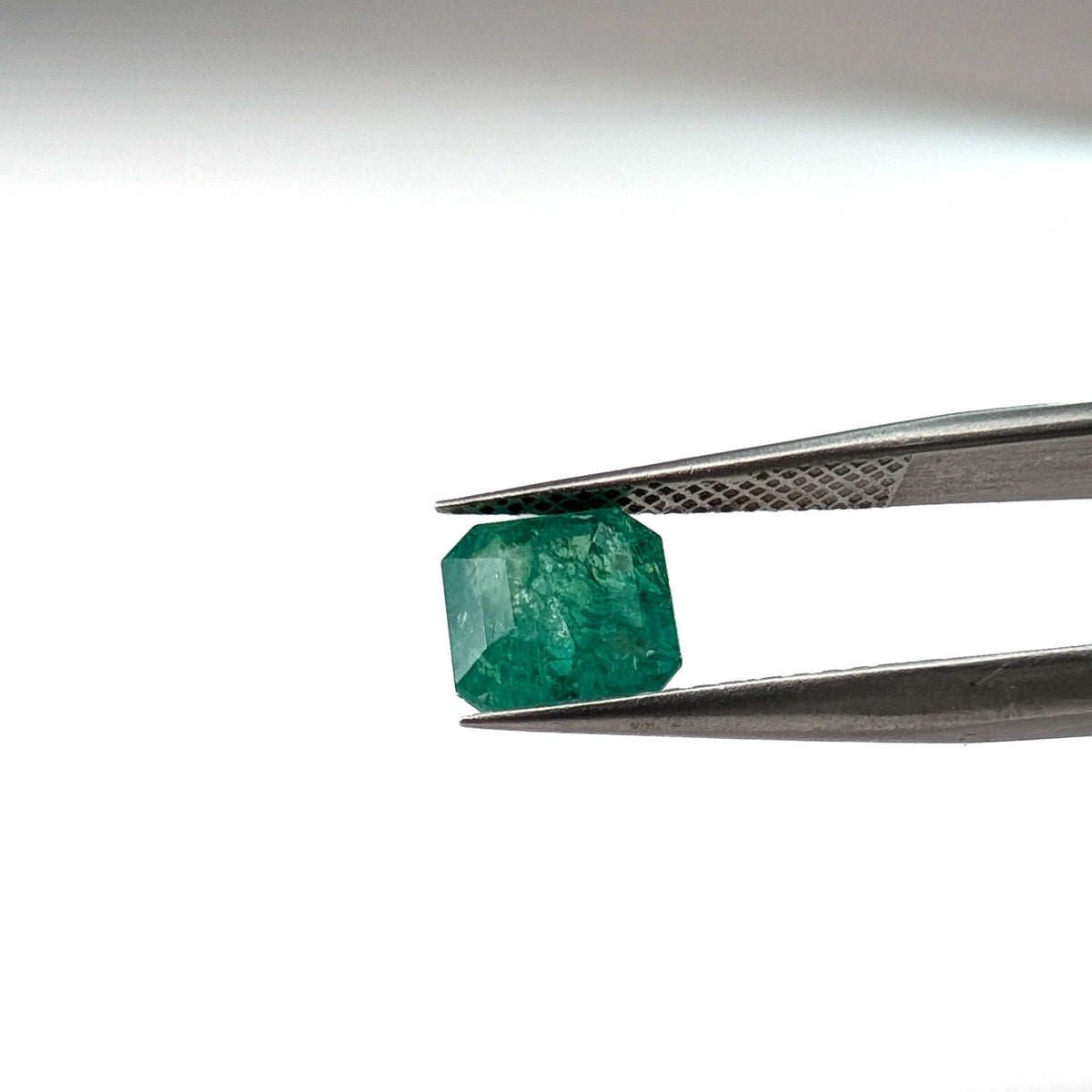 Emerald faceted emerald cut gemstone, 1.53ct, held in tweezers, view 10 of 12