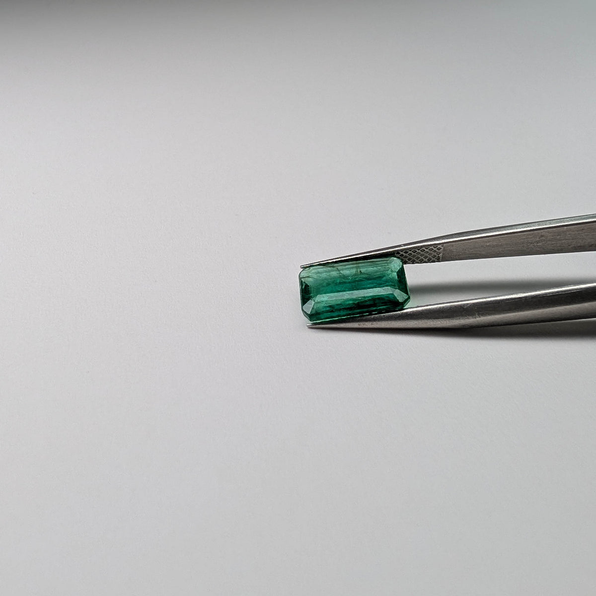Emerald faceted emerald cut gemstone, 2.04ct, held in tweezers, view 10 of 11