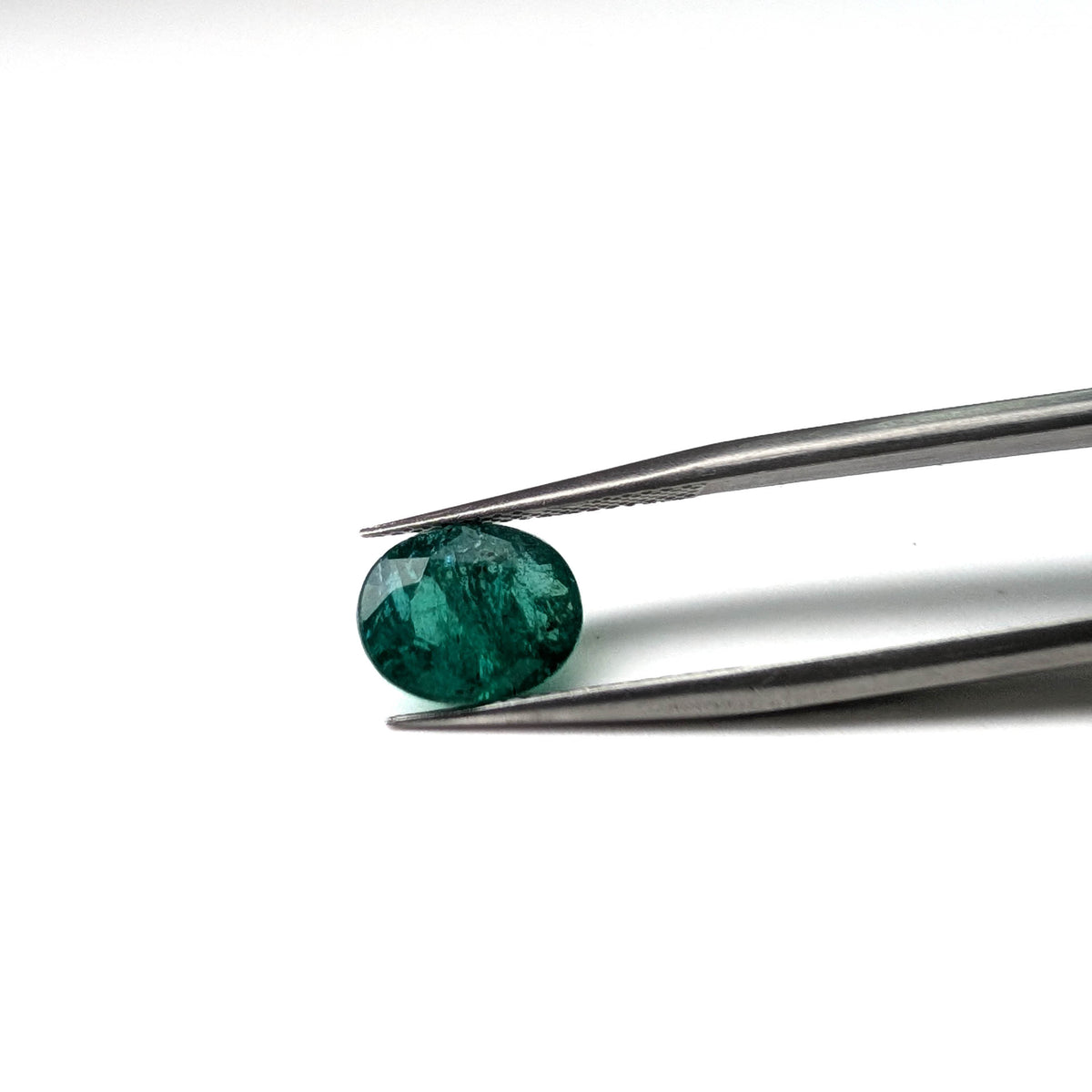 Emerald faceted oval cut gemstone, 2.45ct, held in tweezers, view 2 of 18