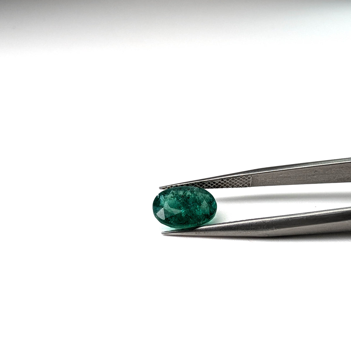 Emerald faceted oval cut gemstone, 2.45ct, held in tweezers, view 16 of 18