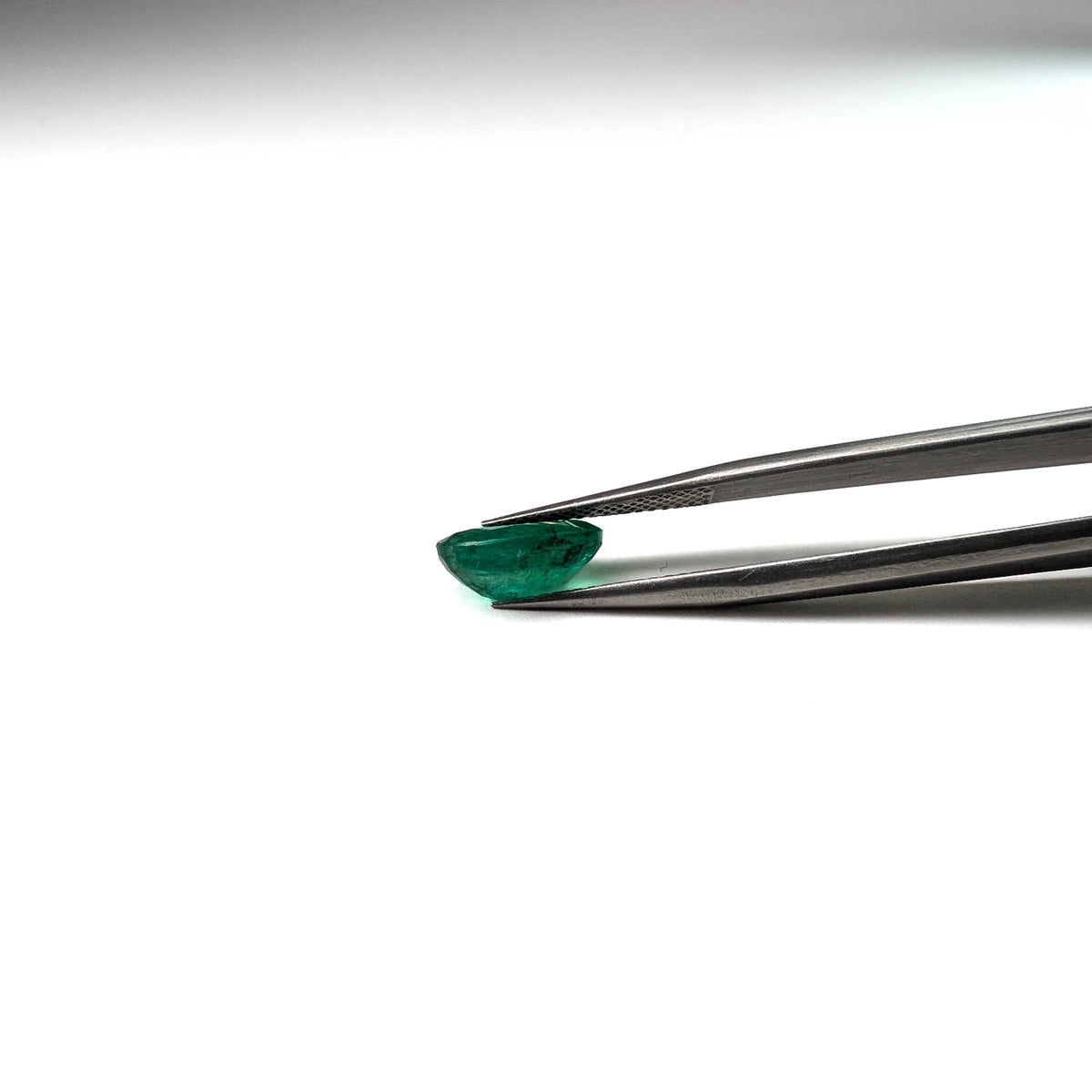 Emerald faceted oval cut gemstone, 2.53ct, held in tweezers, view 13 of 13