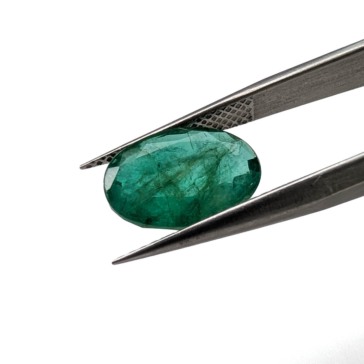 Emerald faceted oval cut gemstone, 3.15ct, held in tweezers, view 2 of 13