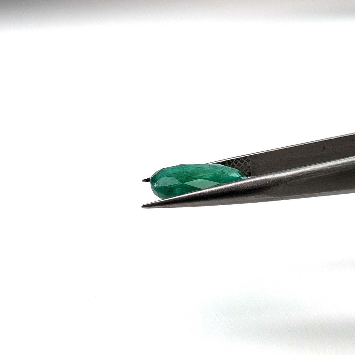 Emerald faceted oval cut gemstone, 3.15ct, held in tweezers, view 8 of 13