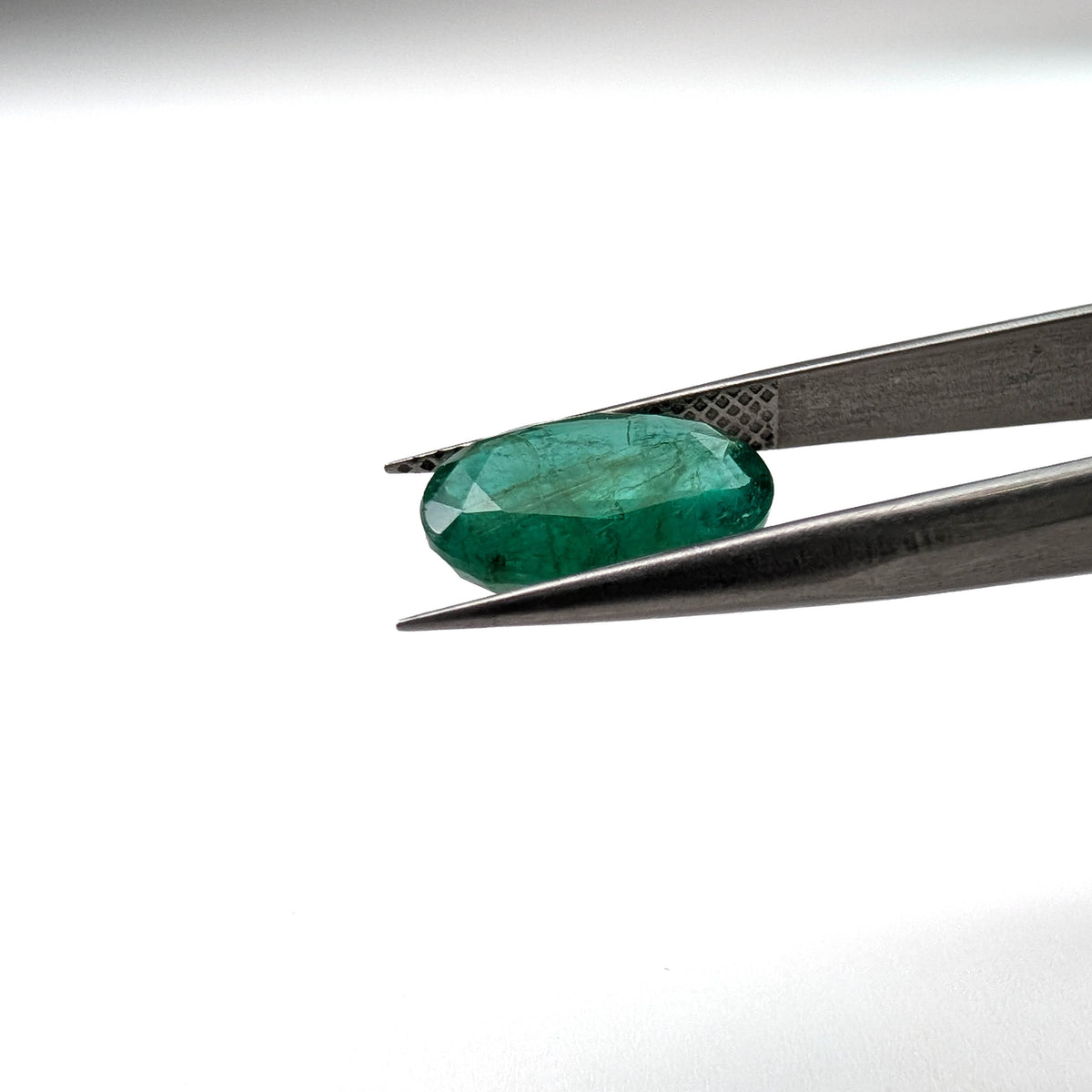 Emerald faceted oval cut gemstone, 3.15ct, held in tweezers, view 10 of 13