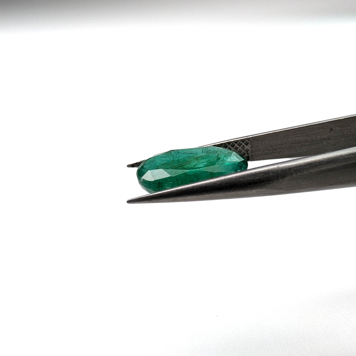 Emerald faceted oval cut gemstone, 3.15ct, held in tweezers, view 11 of 13