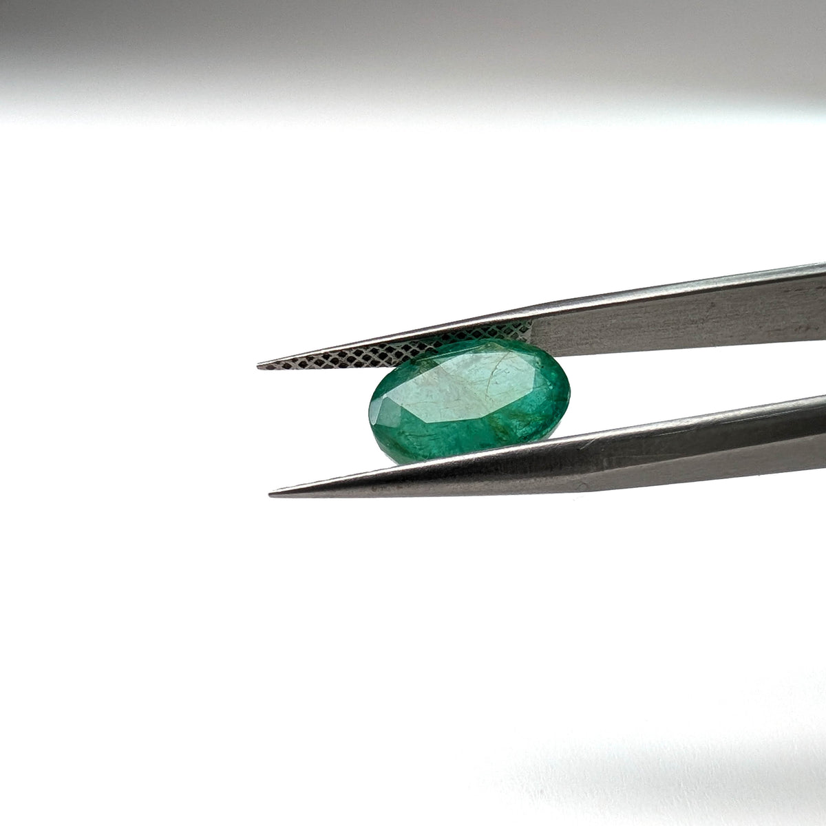 Emerald faceted oval cut gemstone, 3.22ct, held in tweezers, view 2 of 12