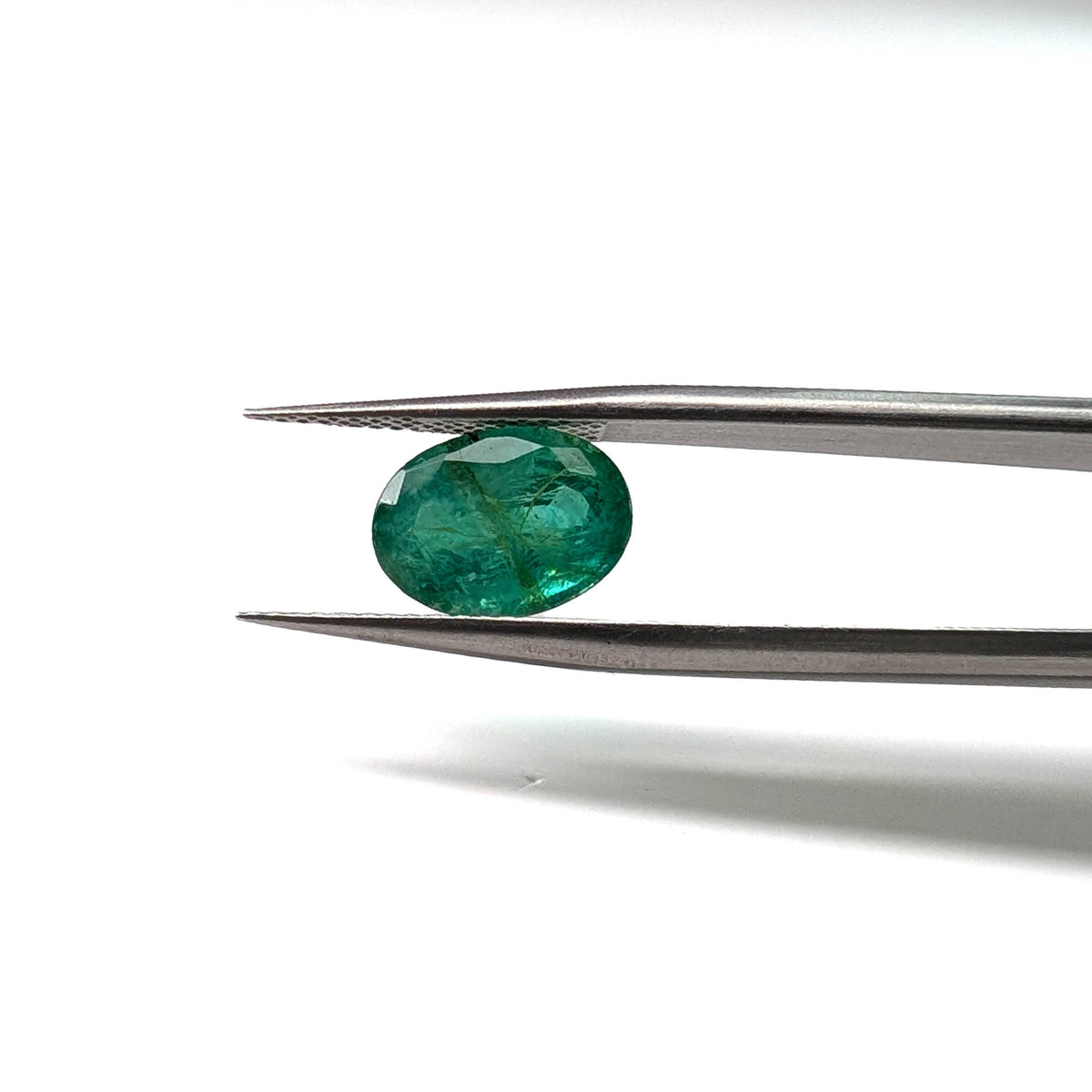 Emerald faceted oval cut gemstone, 3.22ct, held in tweezers, view 11 of 12