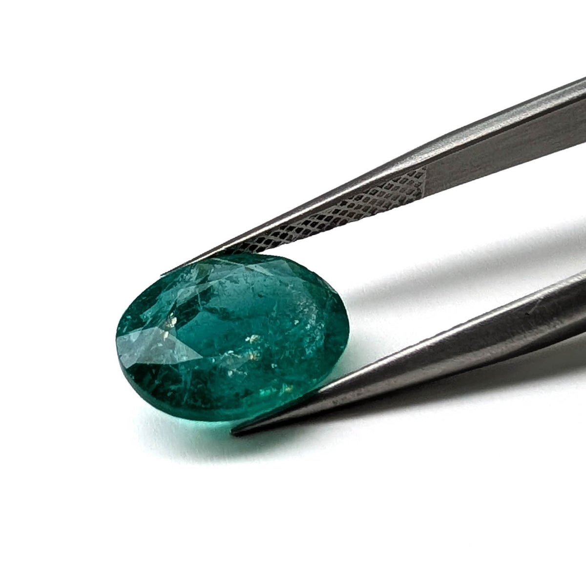 Emerald faceted oval cut gemstone, 3.55ct, held in tweezers, view 2 of 9