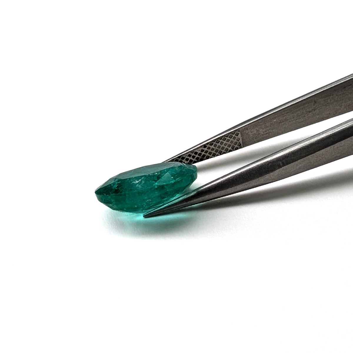 Emerald faceted oval cut gemstone, 3.55ct, held in tweezers, view 7 of 9