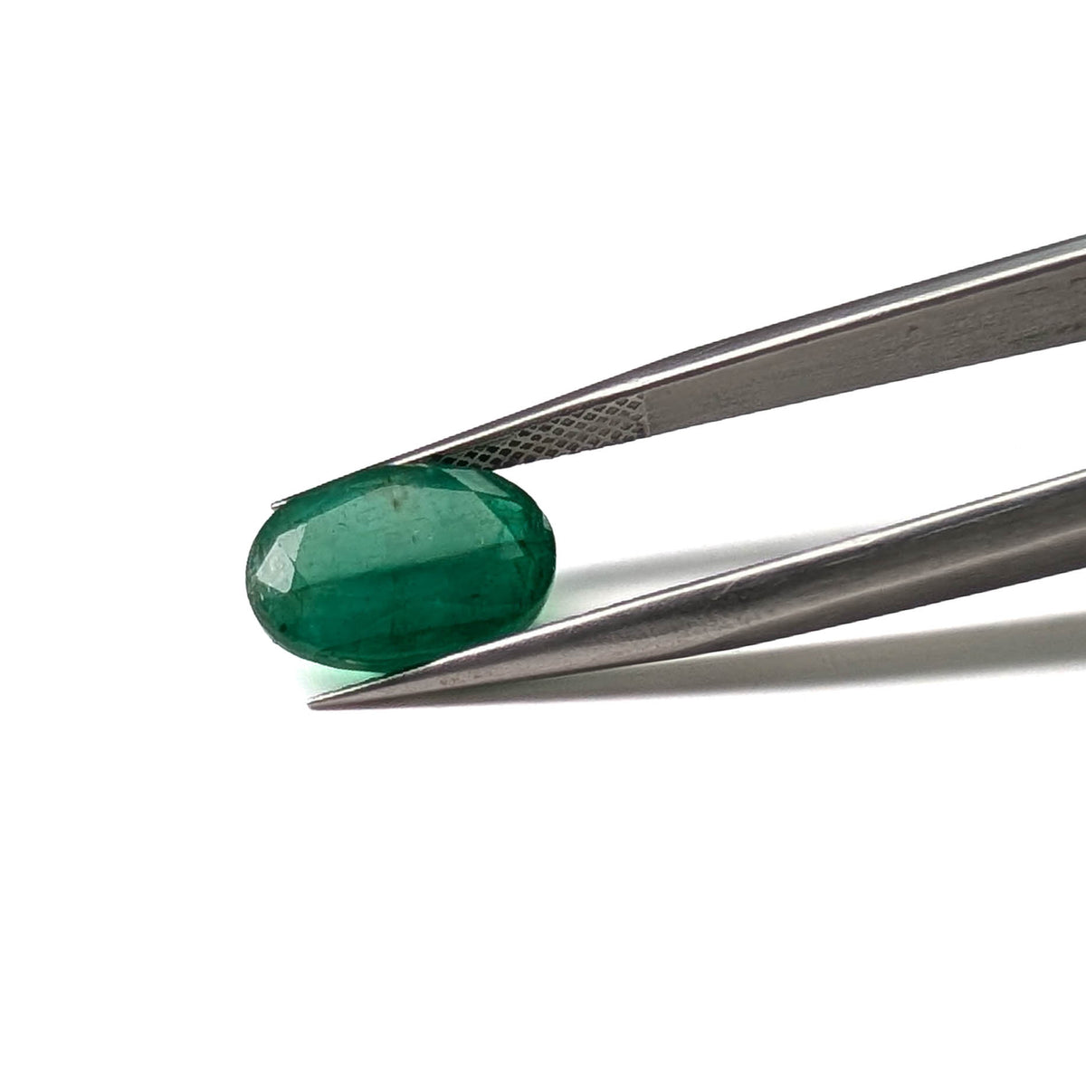 Emerald faceted oval cut gemstone, 3.84ct, held in tweezers, view 2 of 9