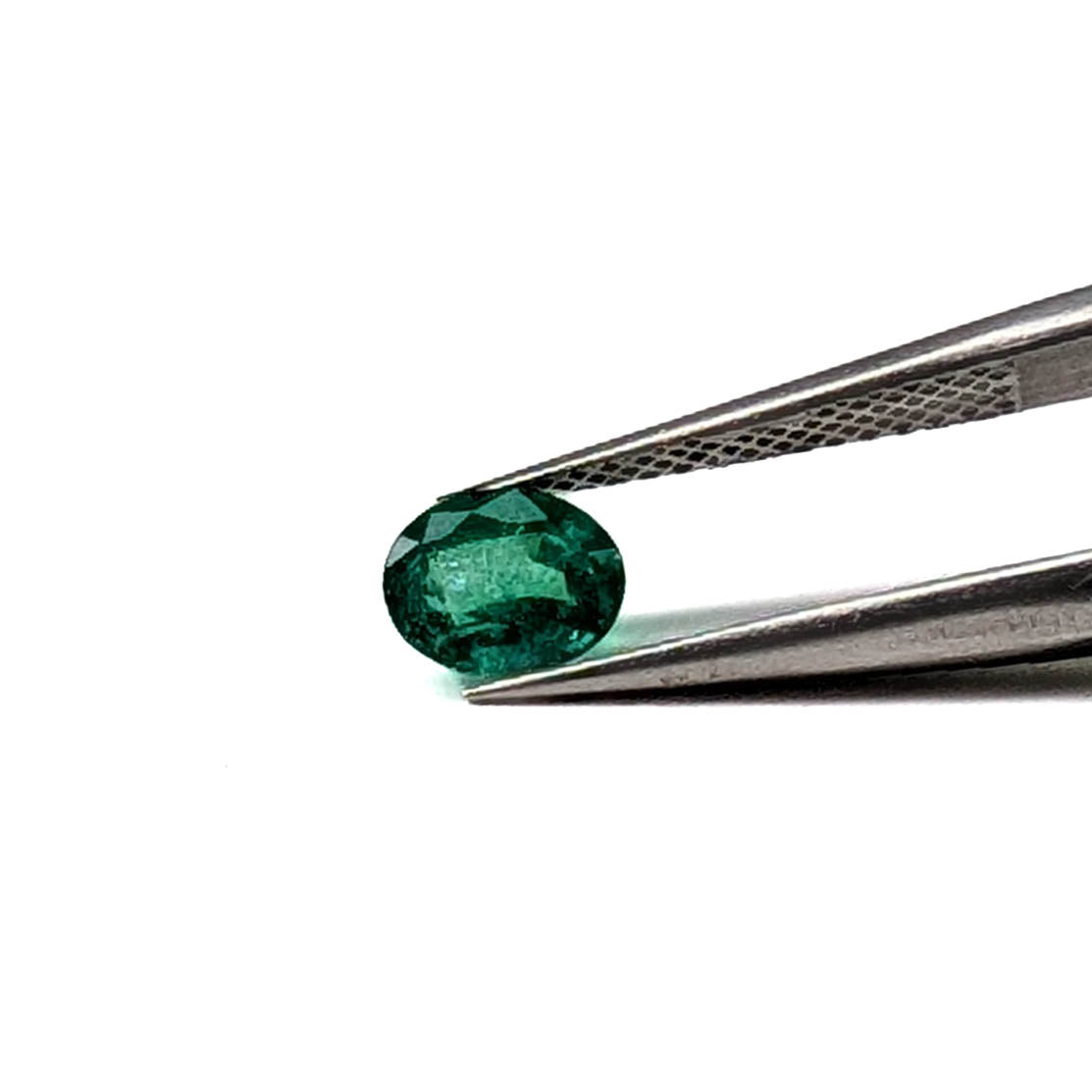 Emerald faceted oval gemstone, 0.73ct, held in tweezers, face-up, view 2 of 10