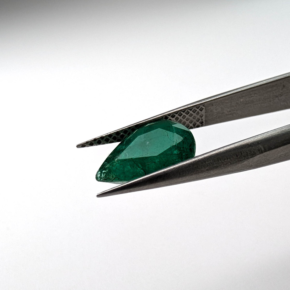 Emerald faceted pear cut gemstone, 2.66ct, held in tweezers, view 12 of 13