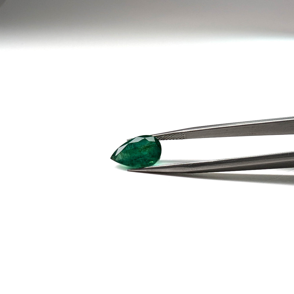 Emerald faceted pear cut gemstone, 3.92ct, held in tweezers, view 10 of 12