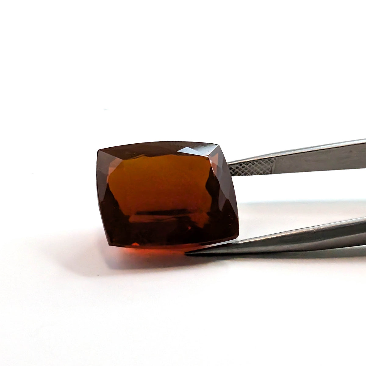 Fire Opal faceted cushion gemstone, 13.61ct, held in tweezers