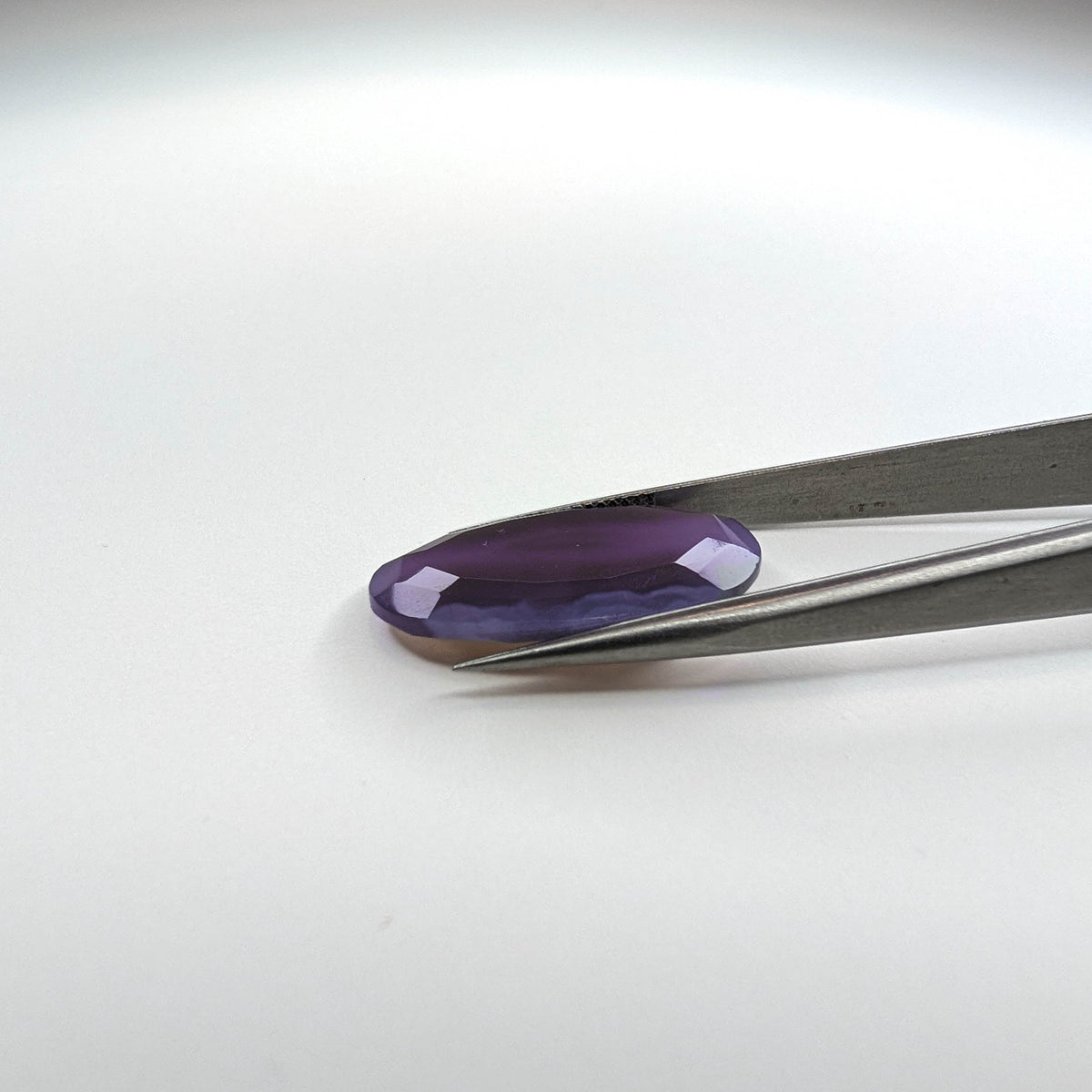 Holly Blue agate faceted egg step tablet cut gemstone, 14.08ct, from Holley, Oregon, held in tweezers, view 8 of 9