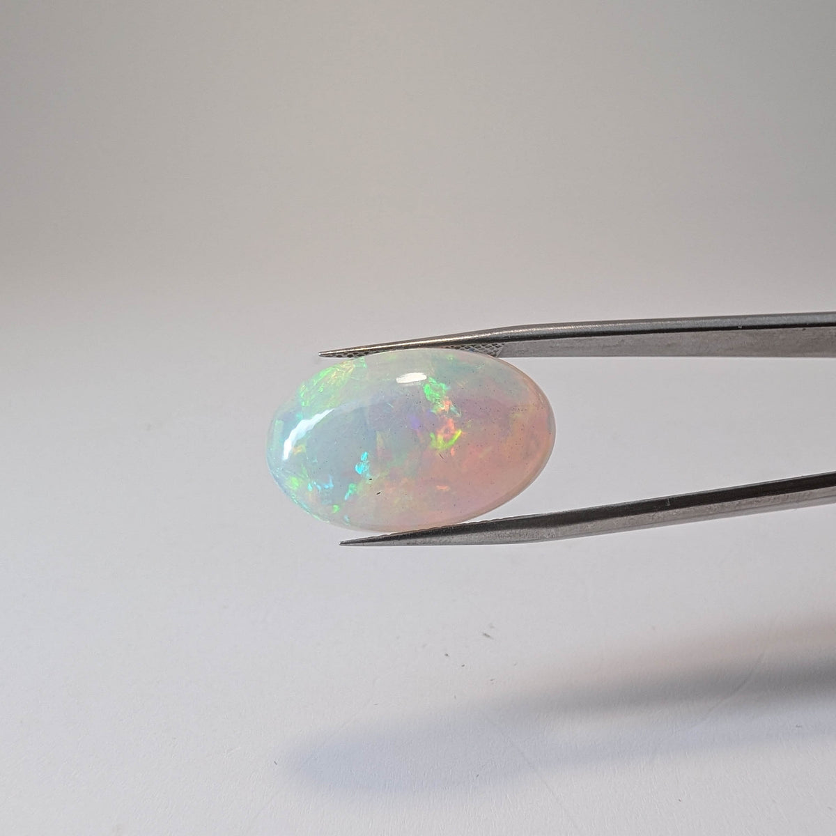 Ethiopian solid opal cabochon oval gemstone, 10.07ct, held in tweezers, view 2 of 8