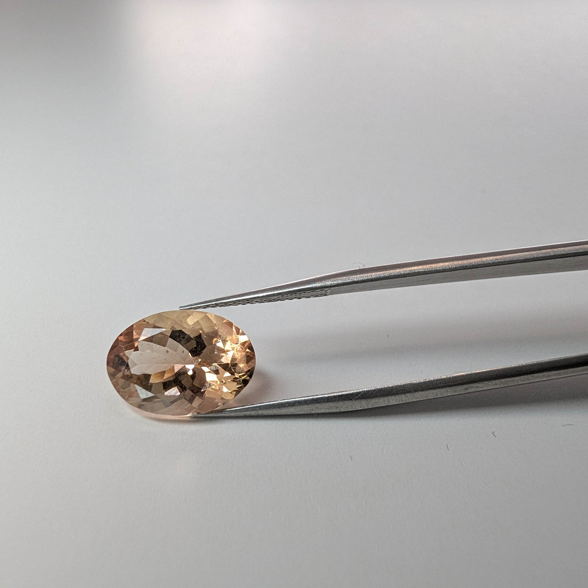 Oregon Sunstone faceted oval cut gemstone, 5.57ct, from Plush, Oregon, held in tweezers, view 2 of 11