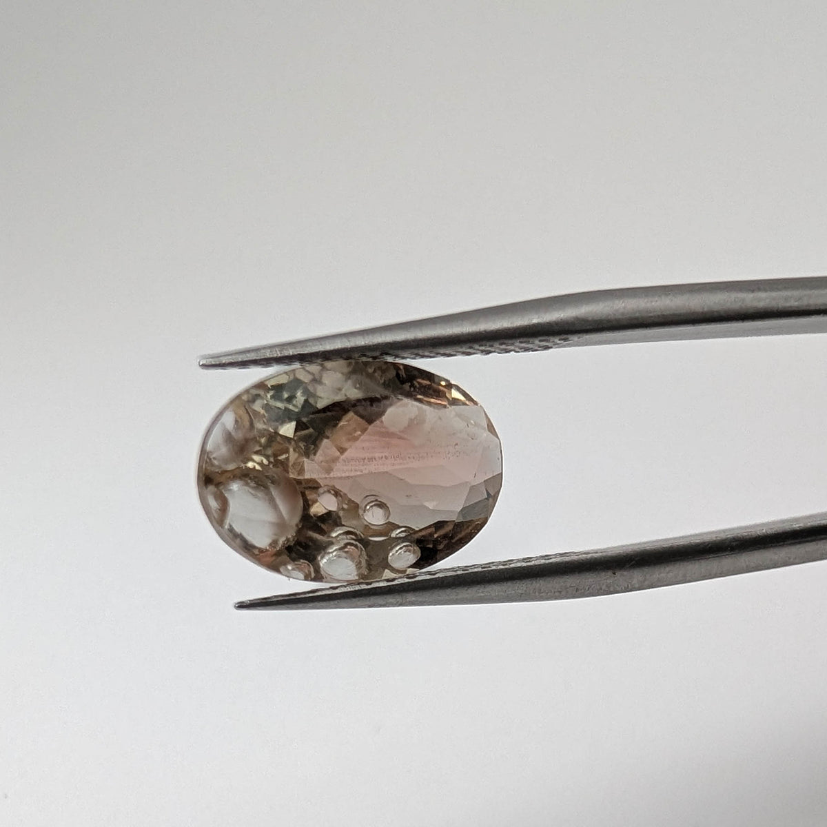 Oregon Sunstone faceted oval fantasy cut gemstone, 3.11ct, from Plush, Oregon, held in tweezers, view 2 of 15