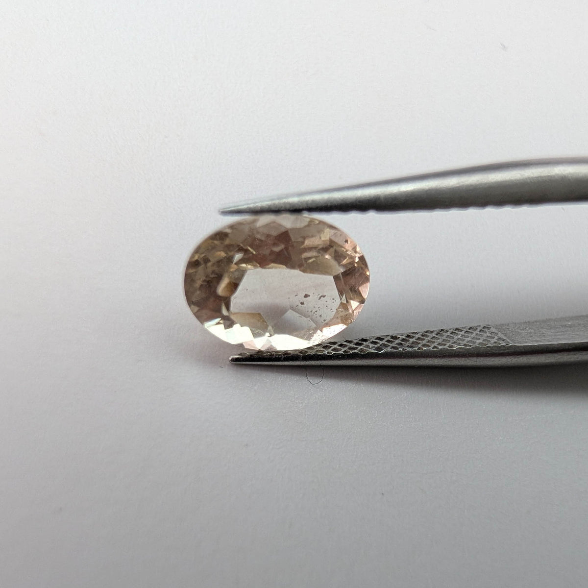Oregon sunstone faceted oval gemstone, 1.70ct, held in tweezers
