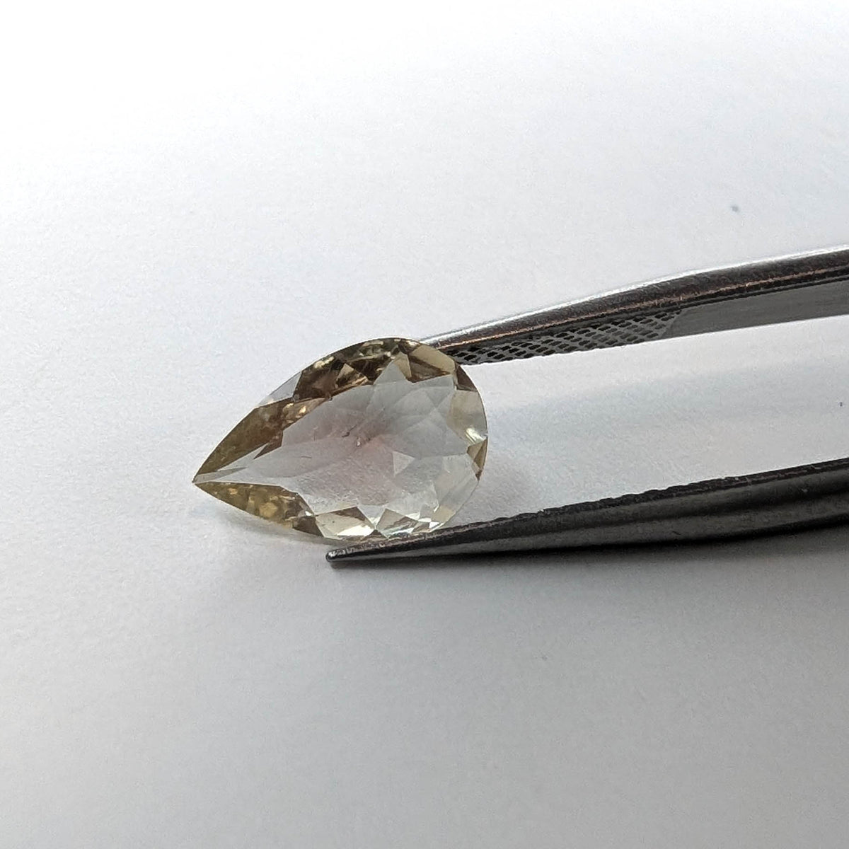Oregon sunstone faceted pear gemstone, 1.30ct, held in tweezers