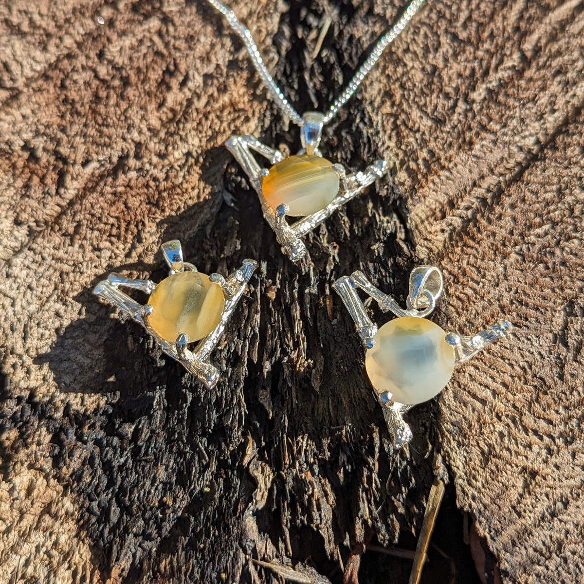 Twig and BC agate pendant in sterling silver – three pendants on wood