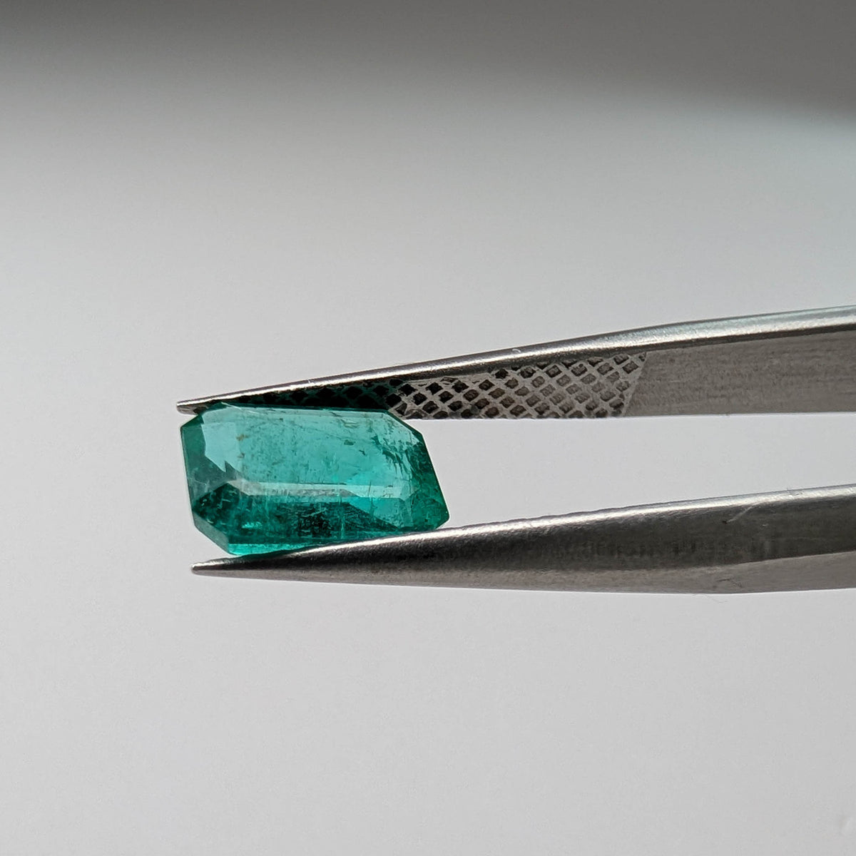 Emerald faceted emerald cut gemstone, 1.09ct, held in tweezers, view 10 of 11