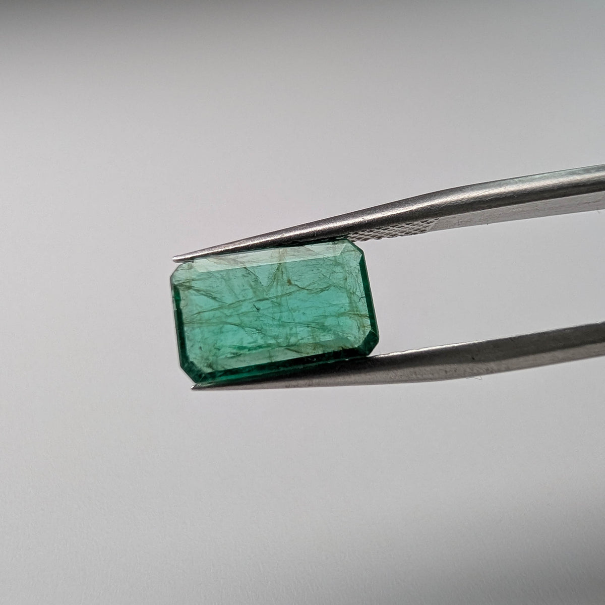 Emerald faceted emerald cut gemstone, 2.04ct, held in tweezers, view 2 of 11