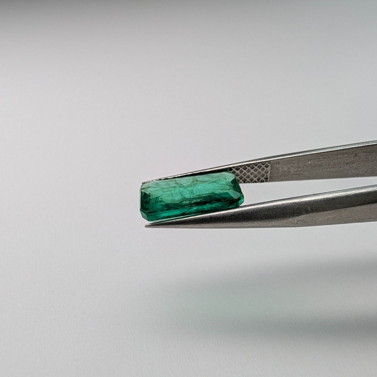 Emerald faceted emerald cut gemstone, 2.04ct, held in tweezers, view 9 of 11