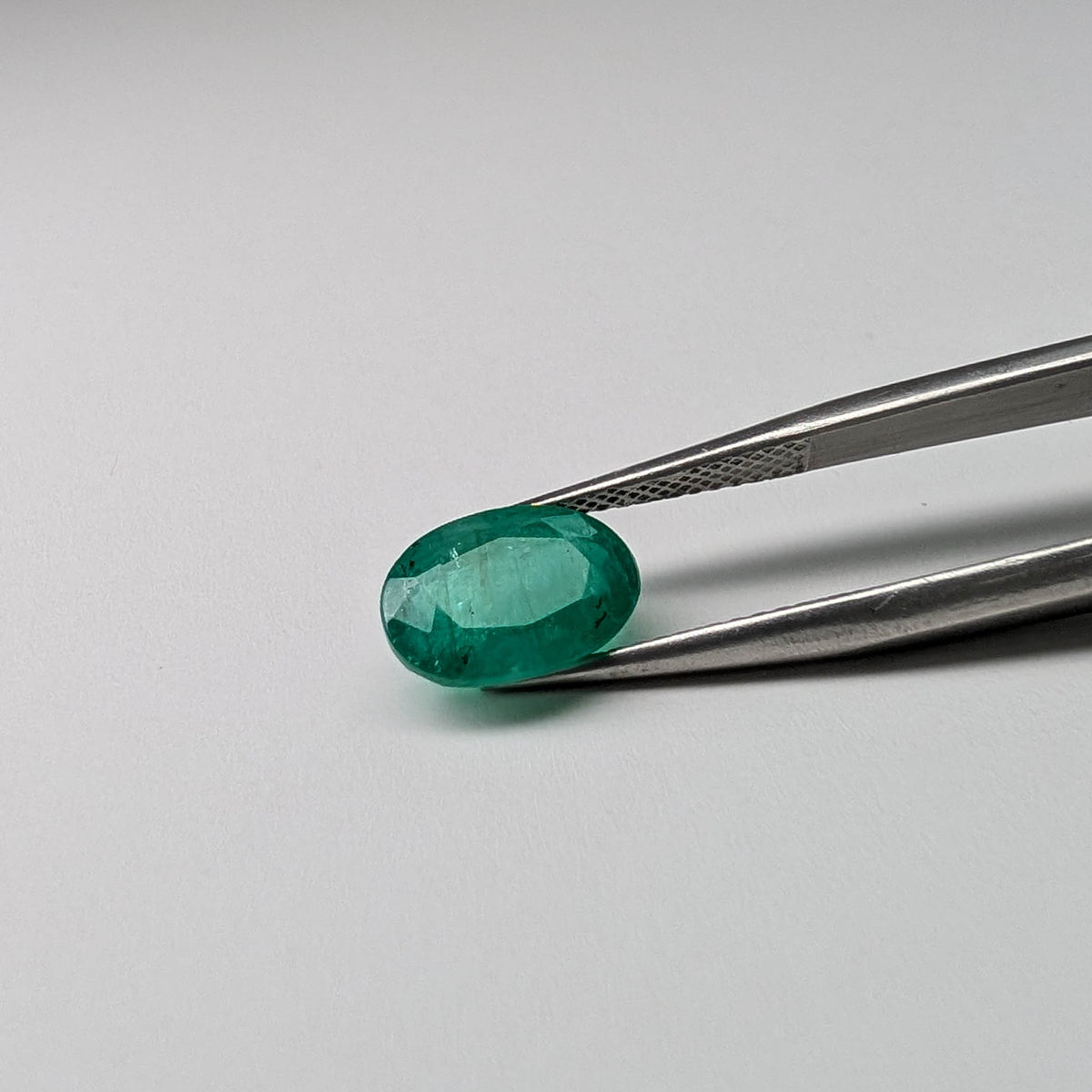 Emerald faceted oval cut gemstone, 2.43ct, held in tweezers, view 2 of 7