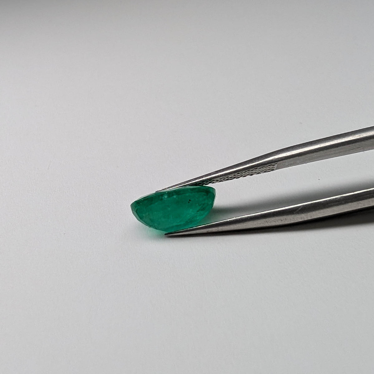 Emerald faceted oval cut gemstone, 2.43ct, held in tweezers, view 7 of 7