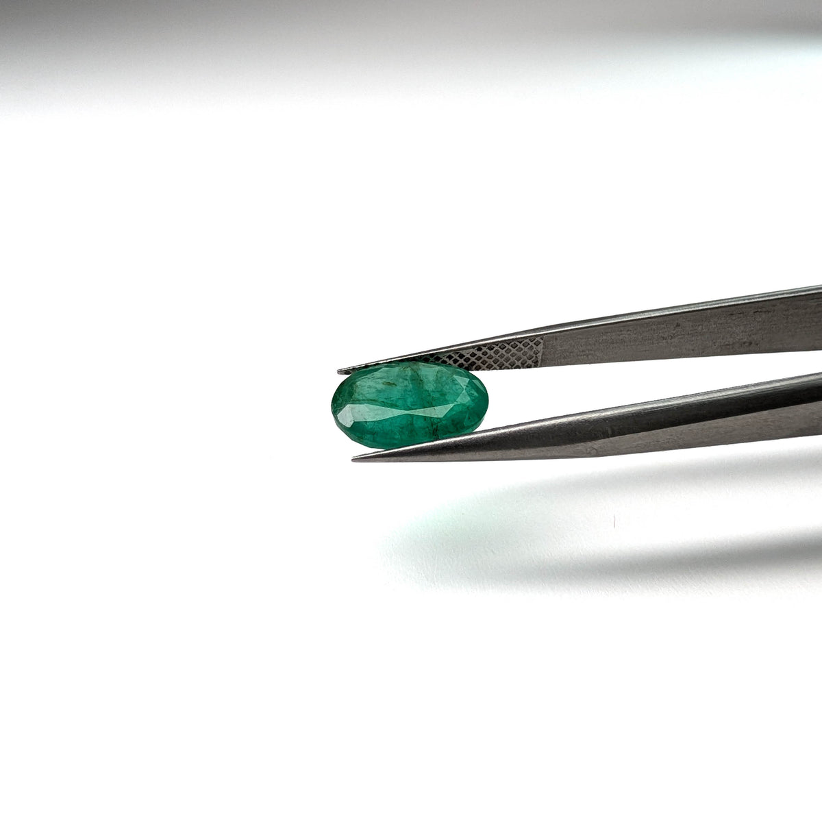 Emerald faceted oval cut gemstone, 2.53ct, held in tweezers, view 2 of 13