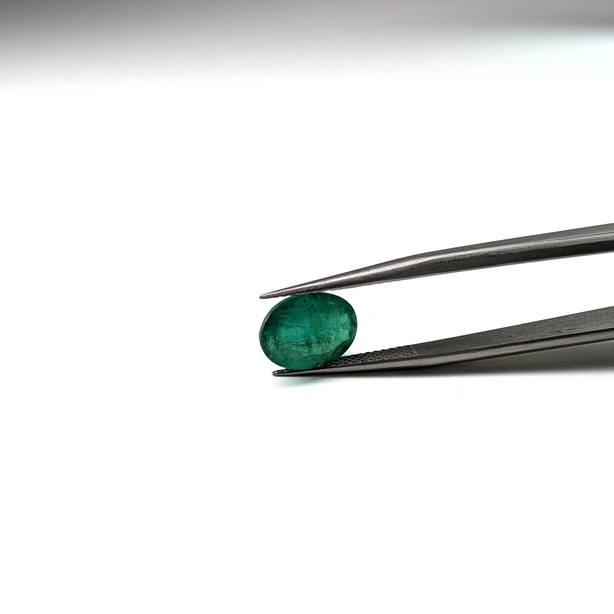 Emerald faceted oval cut gemstone, 2.53ct, held in tweezers, view 12 of 13