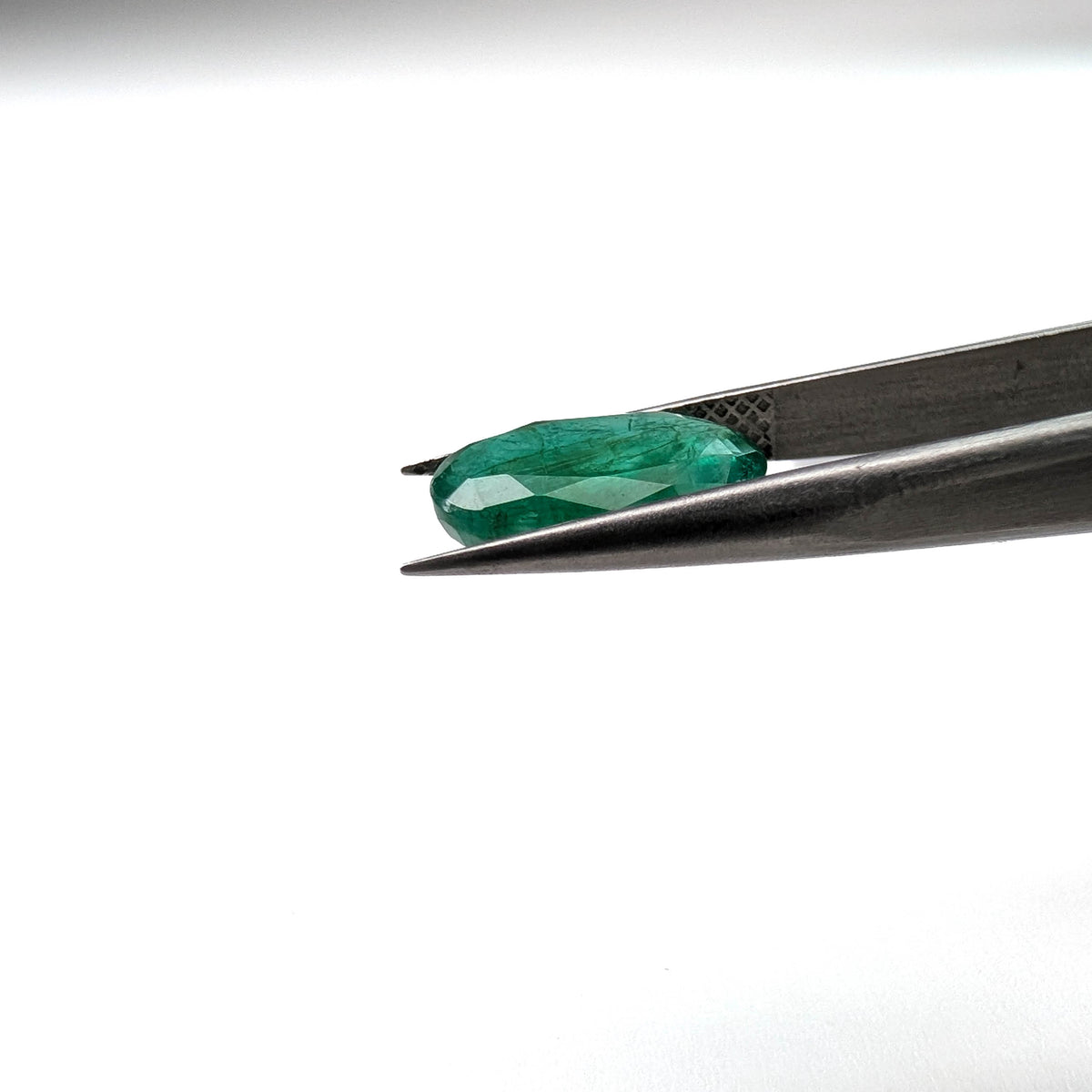 Emerald faceted oval cut gemstone, 3.15ct, held in tweezers, view 9 of 13