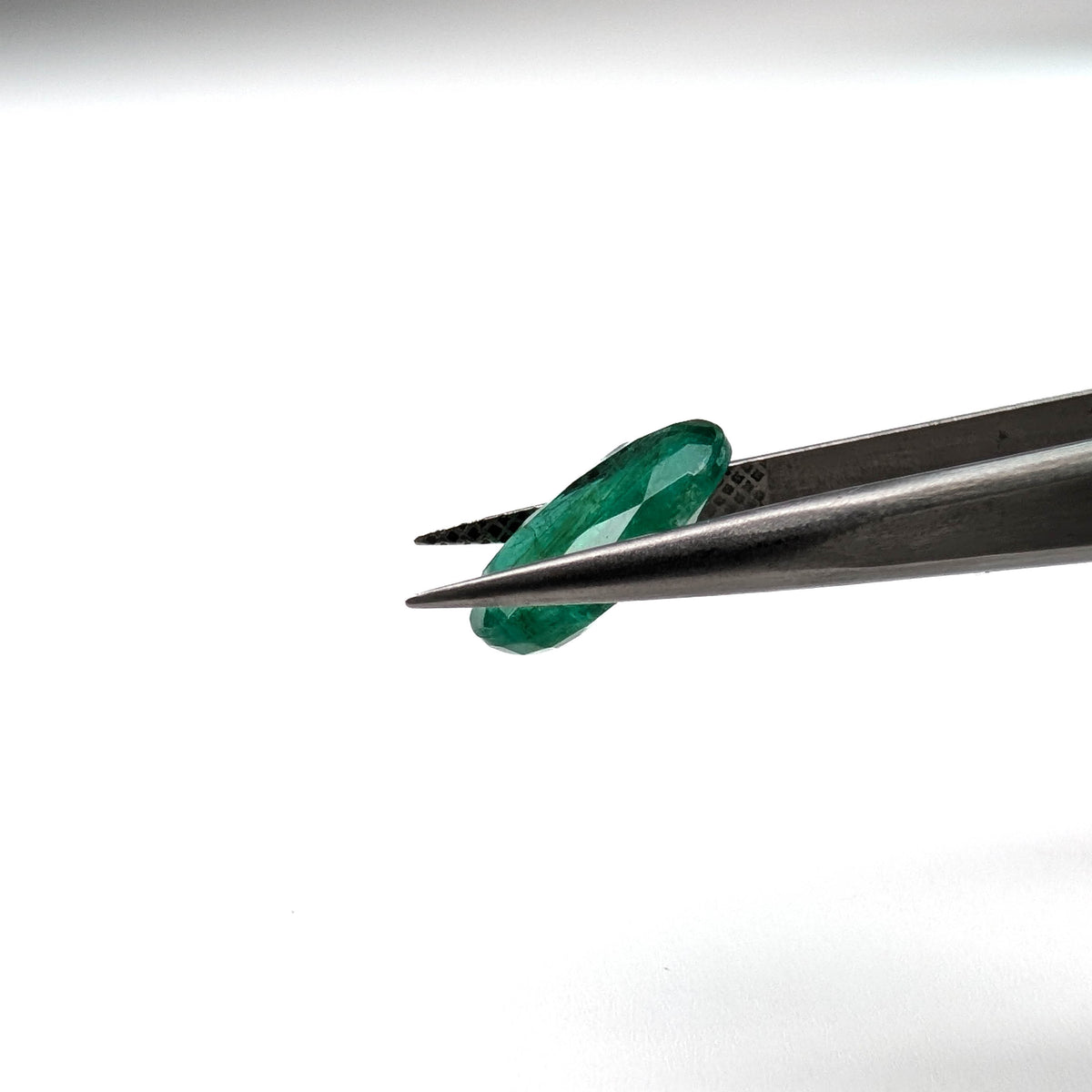 Emerald faceted oval cut gemstone, 3.15ct, held in tweezers, view 12 of 13