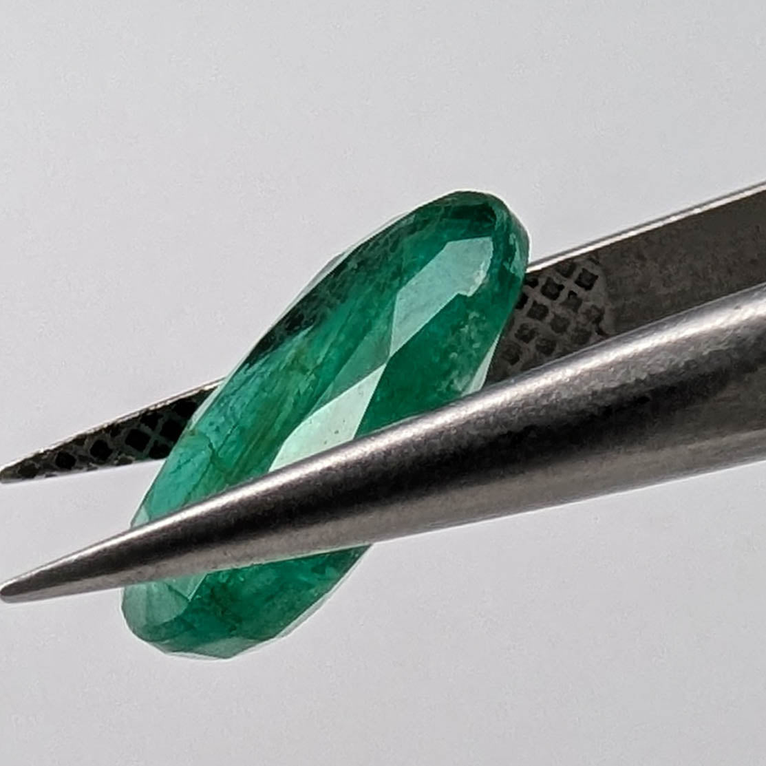 Emerald faceted oval cut gemstone, 3.15ct, held in tweezers, view 13 of 13