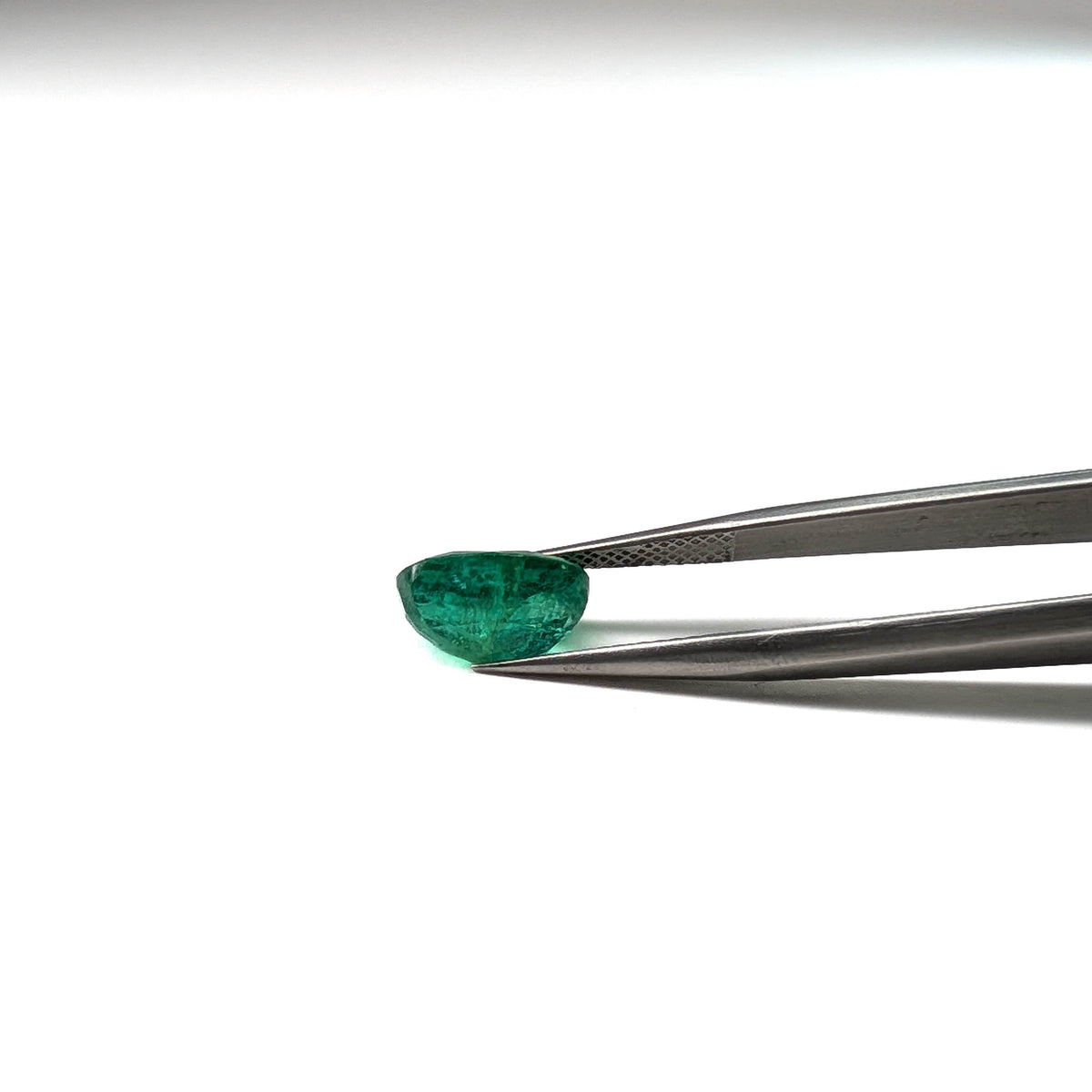Emerald faceted oval cut gemstone, 3.22ct, held in tweezers, view 12 of 12