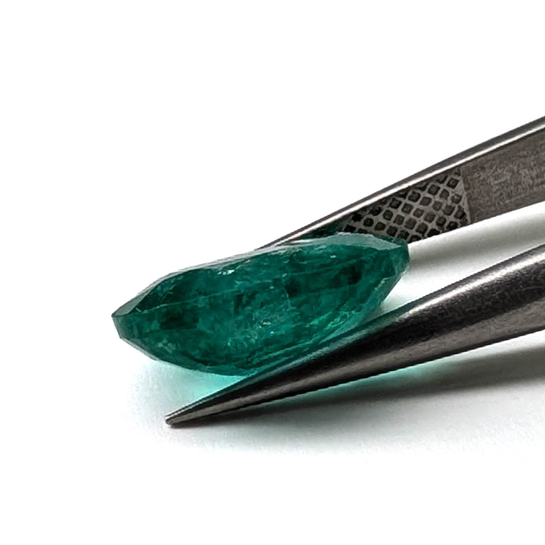 Emerald faceted oval cut gemstone, 3.55ct, held in tweezers, view 9 of 9
