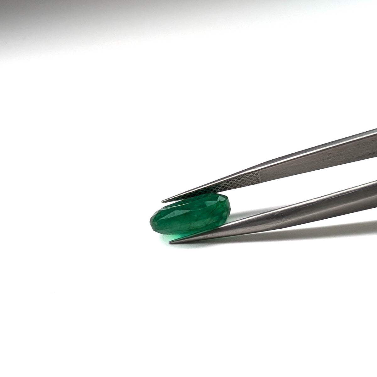 Emerald faceted oval cut gemstone, 3.84ct, held in tweezers, view 7 of 9