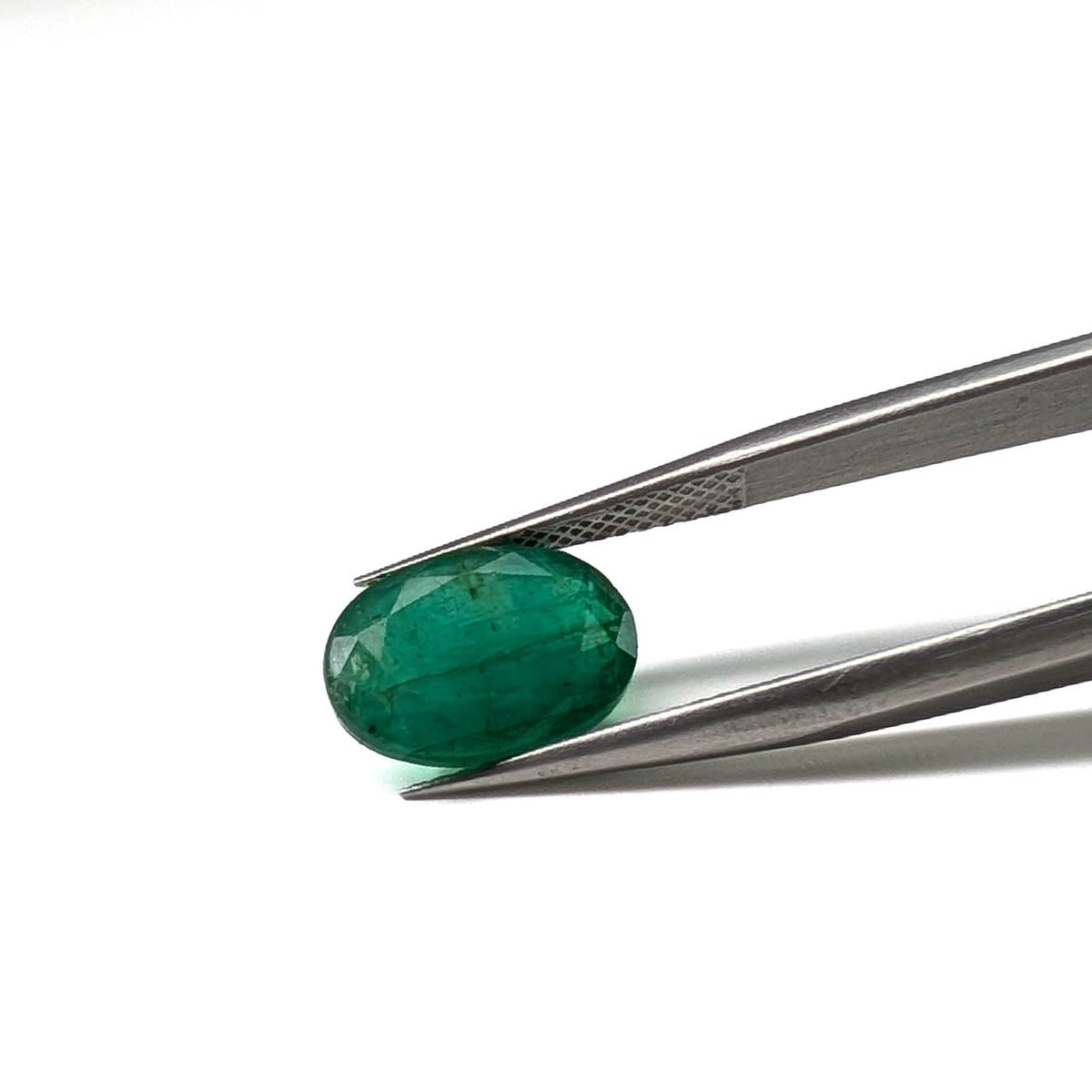 Emerald faceted oval cut gemstone, 3.84ct, held in tweezers, view 8 of 9