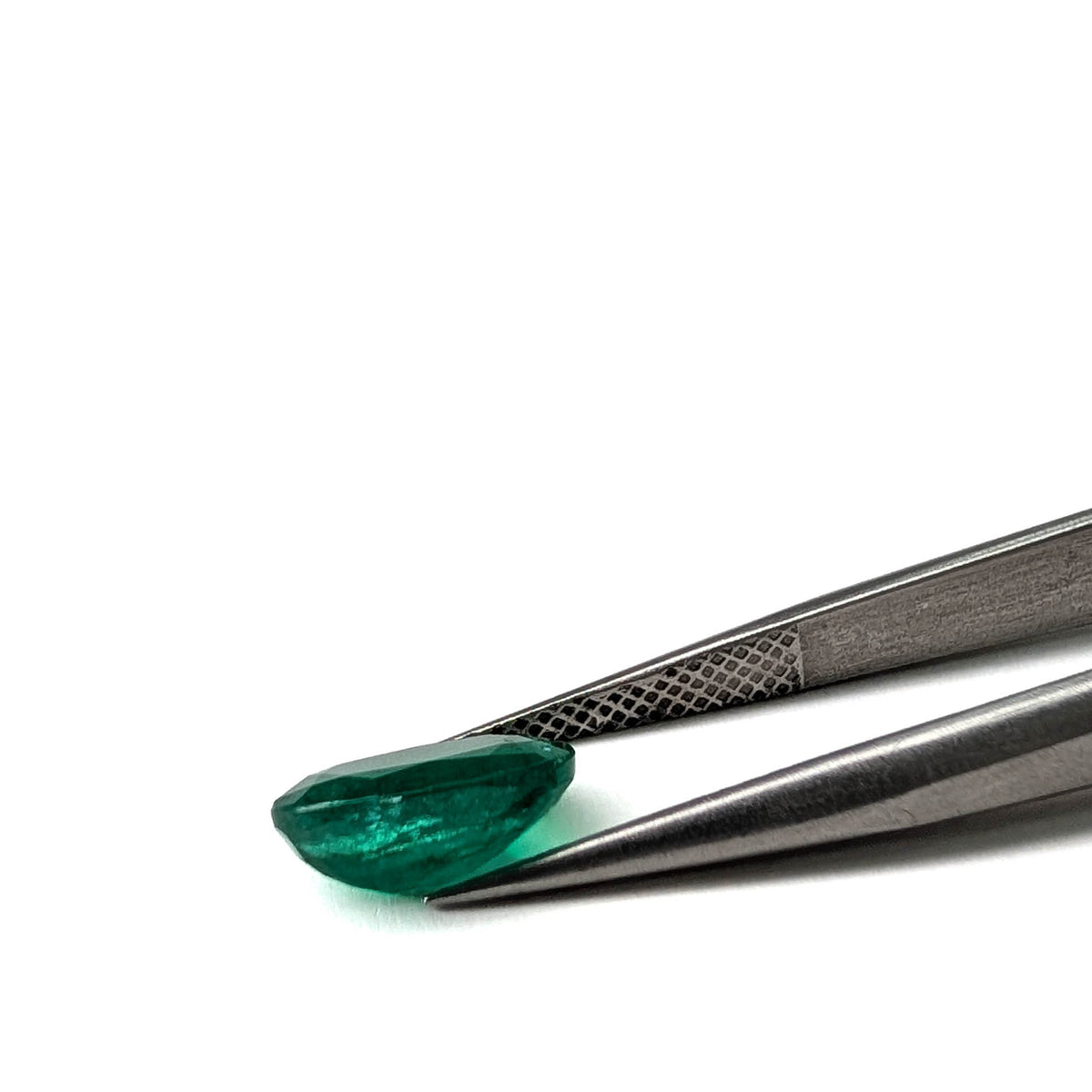 Emerald faceted oval gemstone, 1.92ct, held in tweezers, angled side view, view 12 of 12