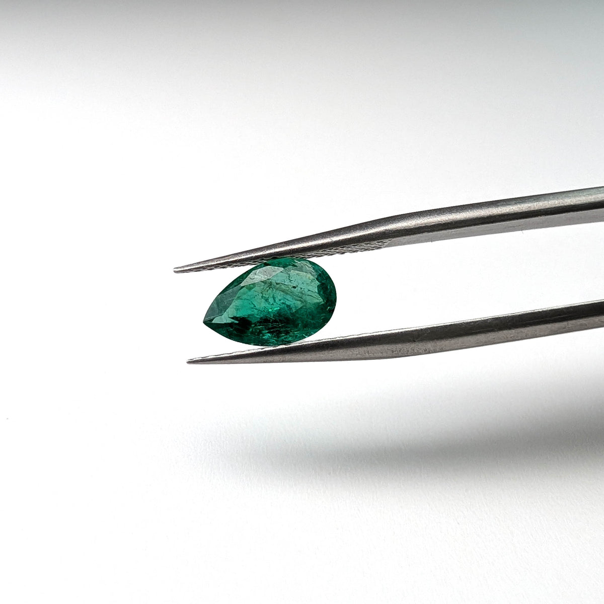 Emerald faceted pear cut gemstone, 0.94ct, held in tweezers, view 2 of 10
