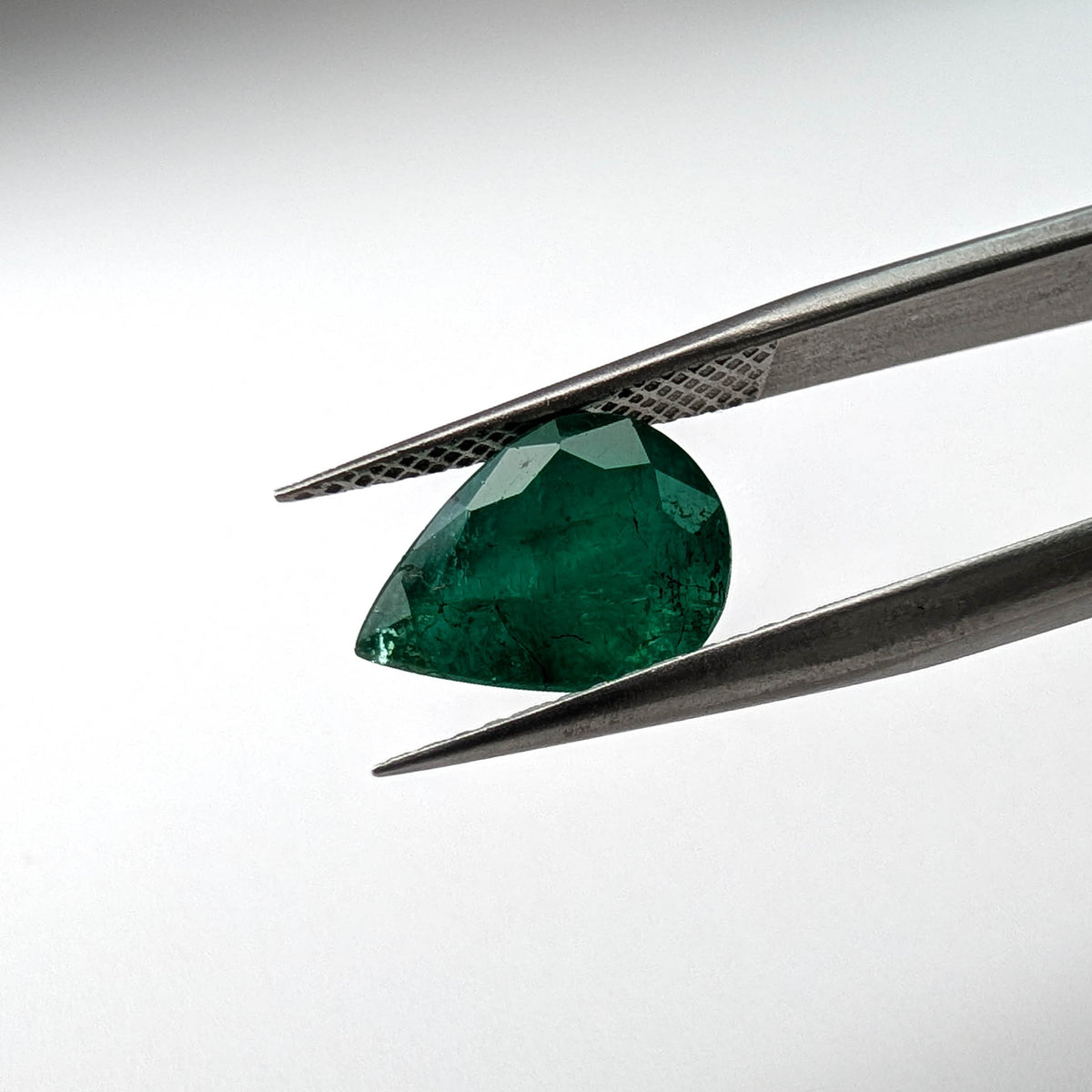 Emerald faceted pear cut gemstone, 2.66ct, held in tweezers, view 2 of 13