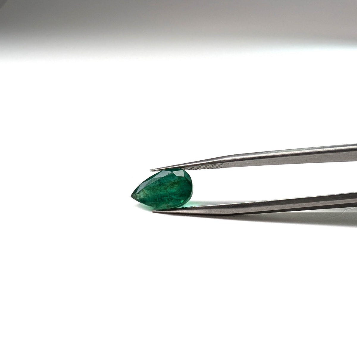 Emerald faceted pear cut gemstone, 3.92ct, held in tweezers, view 2 of 12
