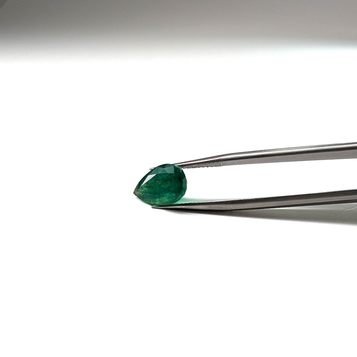 Emerald faceted pear cut gemstone, 3.92ct, held in tweezers, view 11 of 12