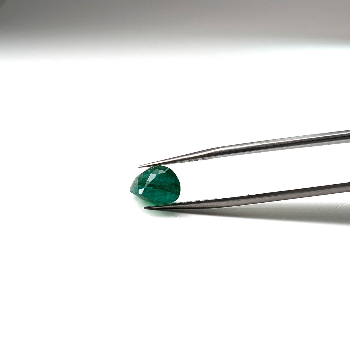 Emerald faceted pear cut gemstone, 3.92ct, held in tweezers, view 12 of 12