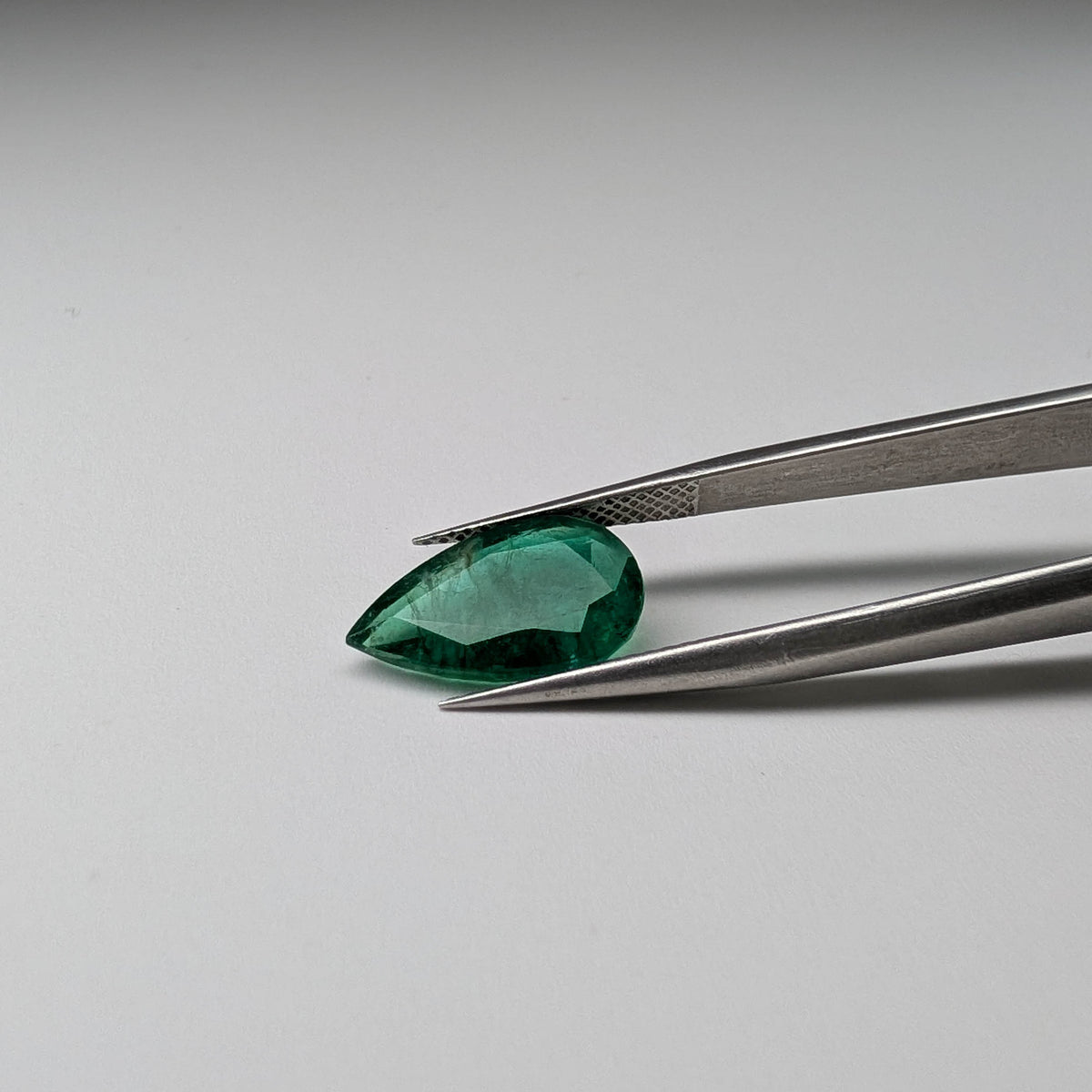 Emerald faceted pear cut gemstone, 3.95ct, held in tweezers, view 12 of 13