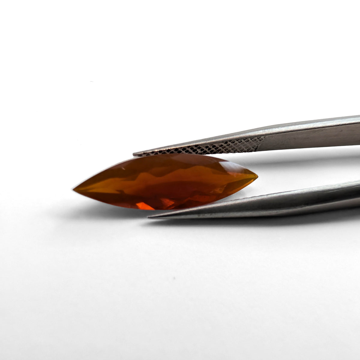 Fire Opal faceted marquise brilliant cut gemstone, 1.88ct, held in tweezers