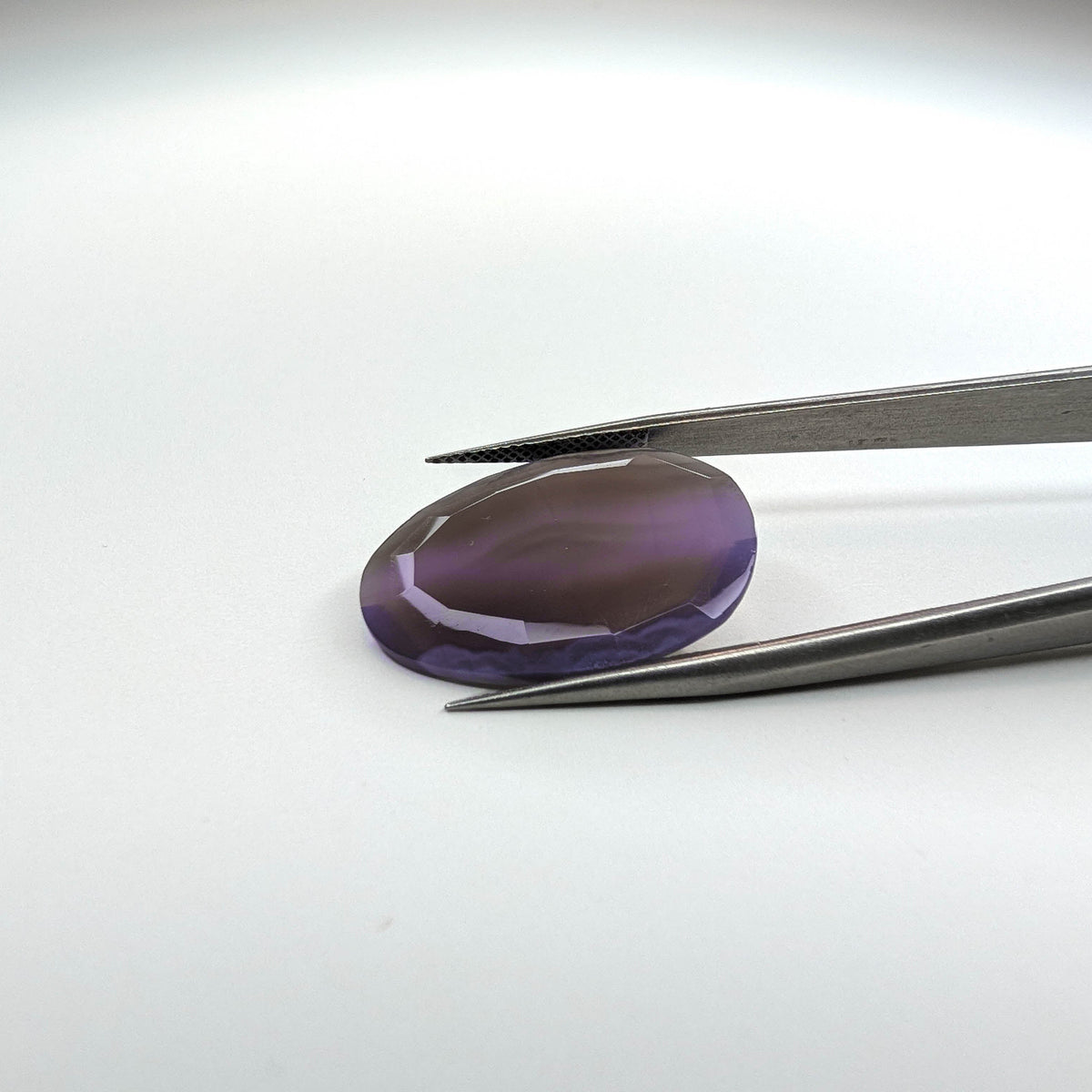 Holly Blue agate faceted egg step tablet cut gemstone, 14.08ct, from Holley, Oregon, held in tweezers, view 2 of 9
