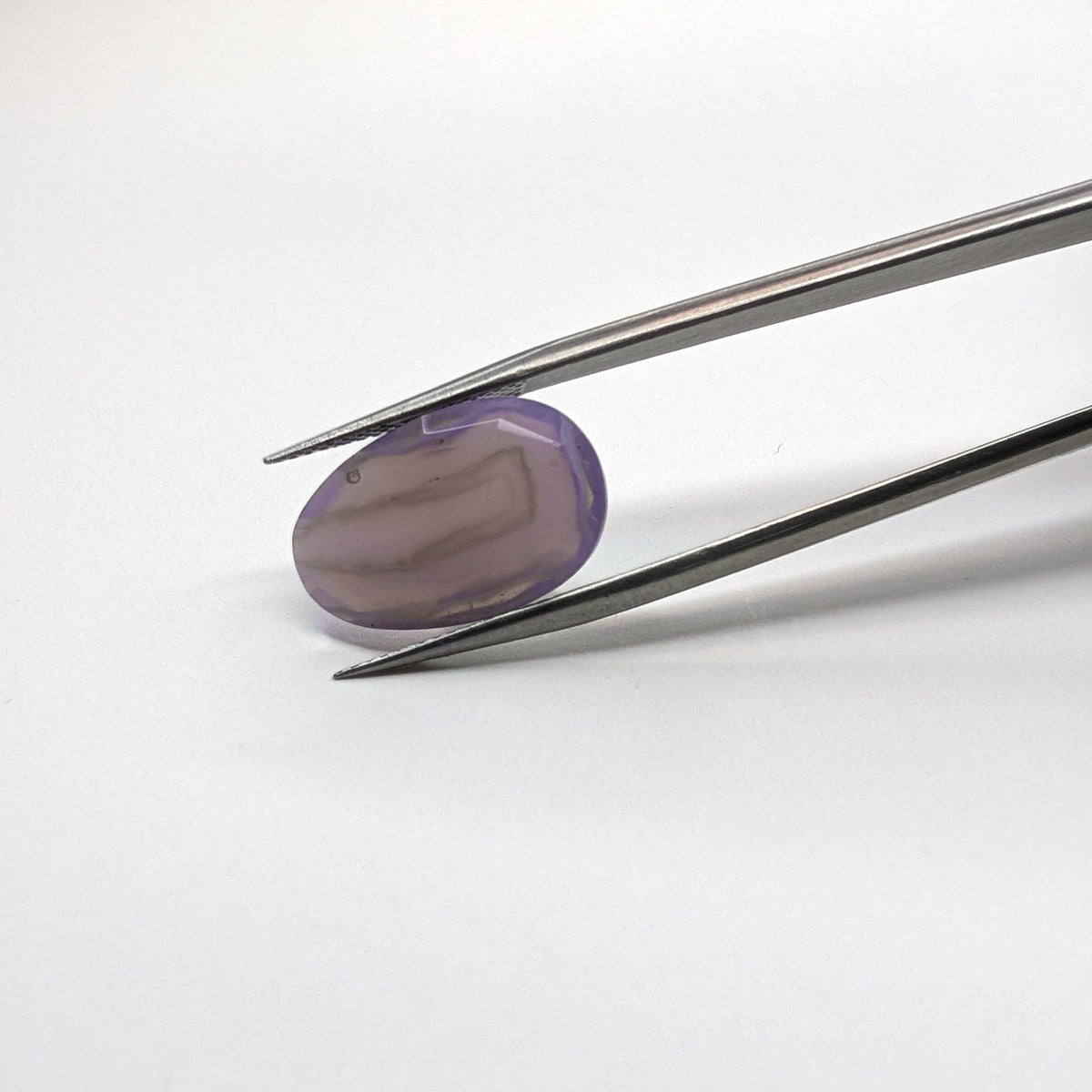 Holly Blue agate faceted egg step tablet cut gemstone, 6.32ct, from Holley, Oregon, held in tweezers, view 2 of 10