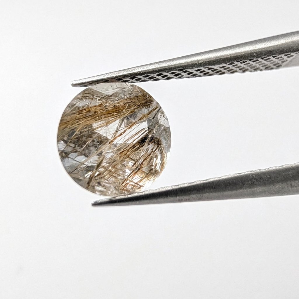 Actinolite quartz faceted round gemstone, 1.18ct, from Mount Breakenridge, Harrison Lake, BC, Canada, held in tweezers, view 2 of 10